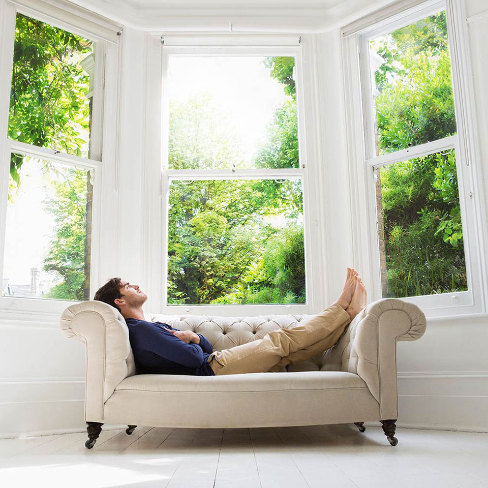 Man Lounging On Sofa By Large Window